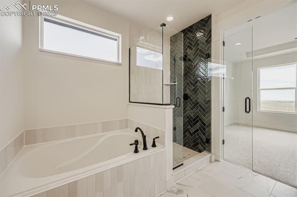 Image 17 of 29: Bathroom with a garden tub, a stall shower, and marble look tiles