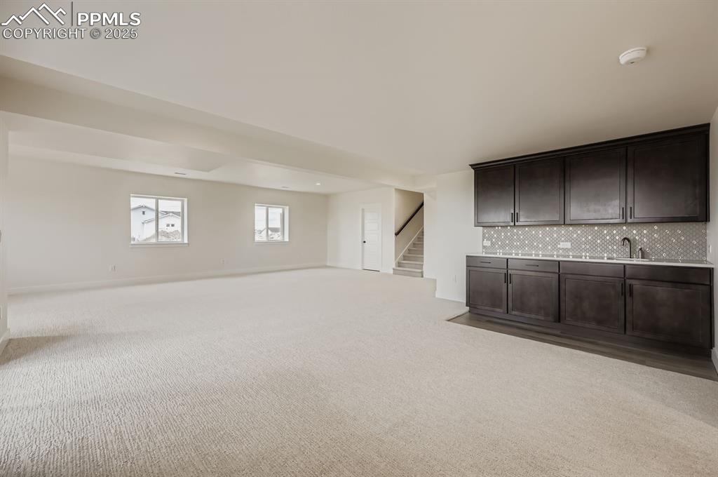 Image 22 of 29: Unfurnished living room with light colored carpet, stairs, and bar with sin