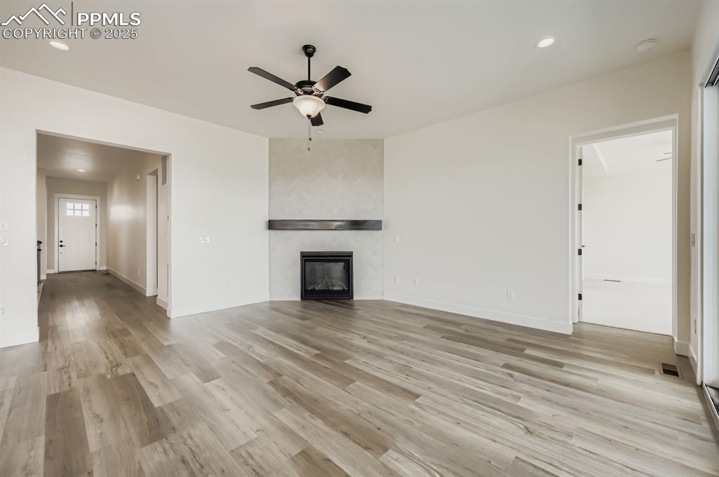 Image 7 of 29: Unfurnished living room with ceiling fan, light wood-style flooring, recess