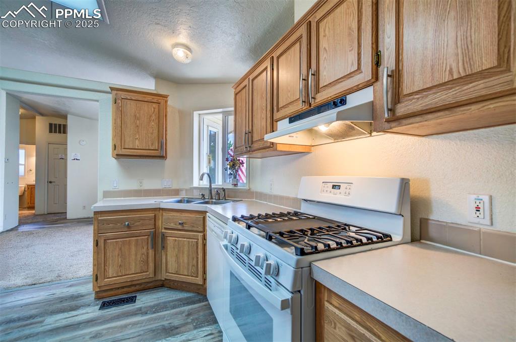 Image 10 of 31: Kitchen featuring white gas stove, under cabinet range hood, light wood-sty