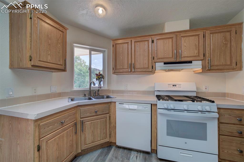Image 12 of 31: Kitchen featuring white appliances, under cabinet range hood, light counter