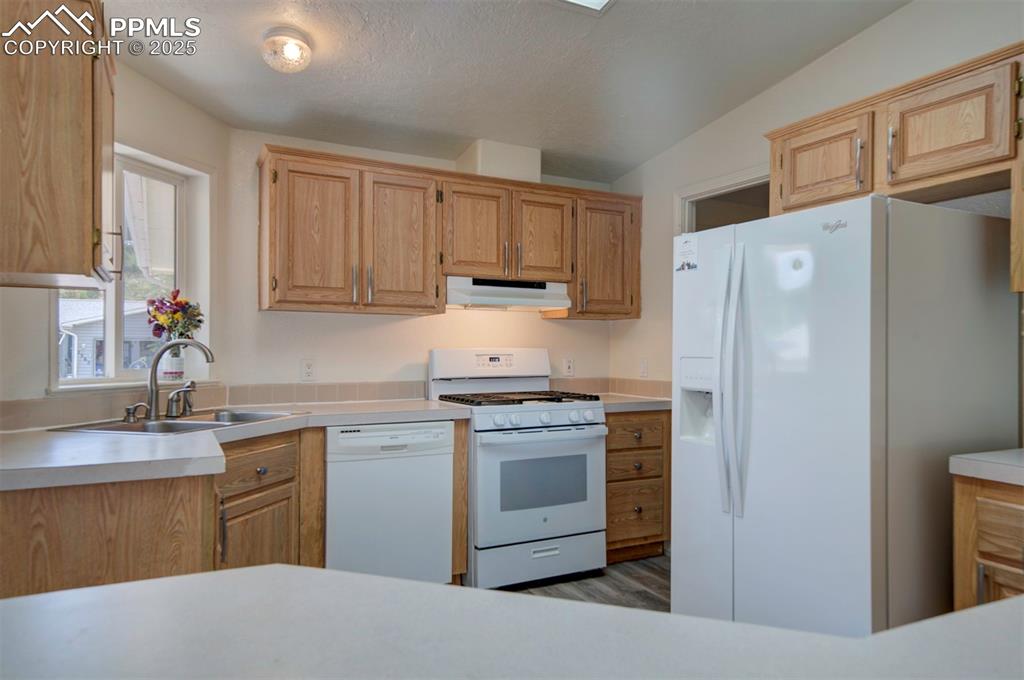 Image 14 of 31: Kitchen featuring white appliances, under cabinet range hood, light counter