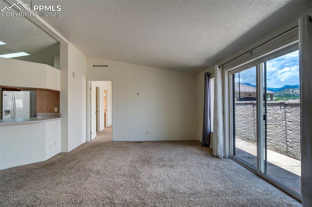 Image 15 of 31: Unfurnished living room with carpet flooring, a textured ceiling, lofted ce
