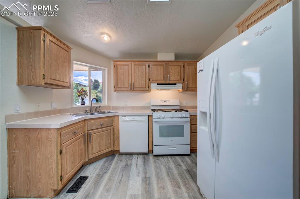 Image 9 of 31: Kitchen with white appliances, under cabinet range hood, light wood finishe