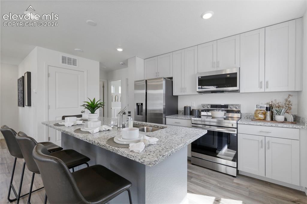 Image 8 of 20: Kitchen featuring a large island with a stone-finish countertop, light wood