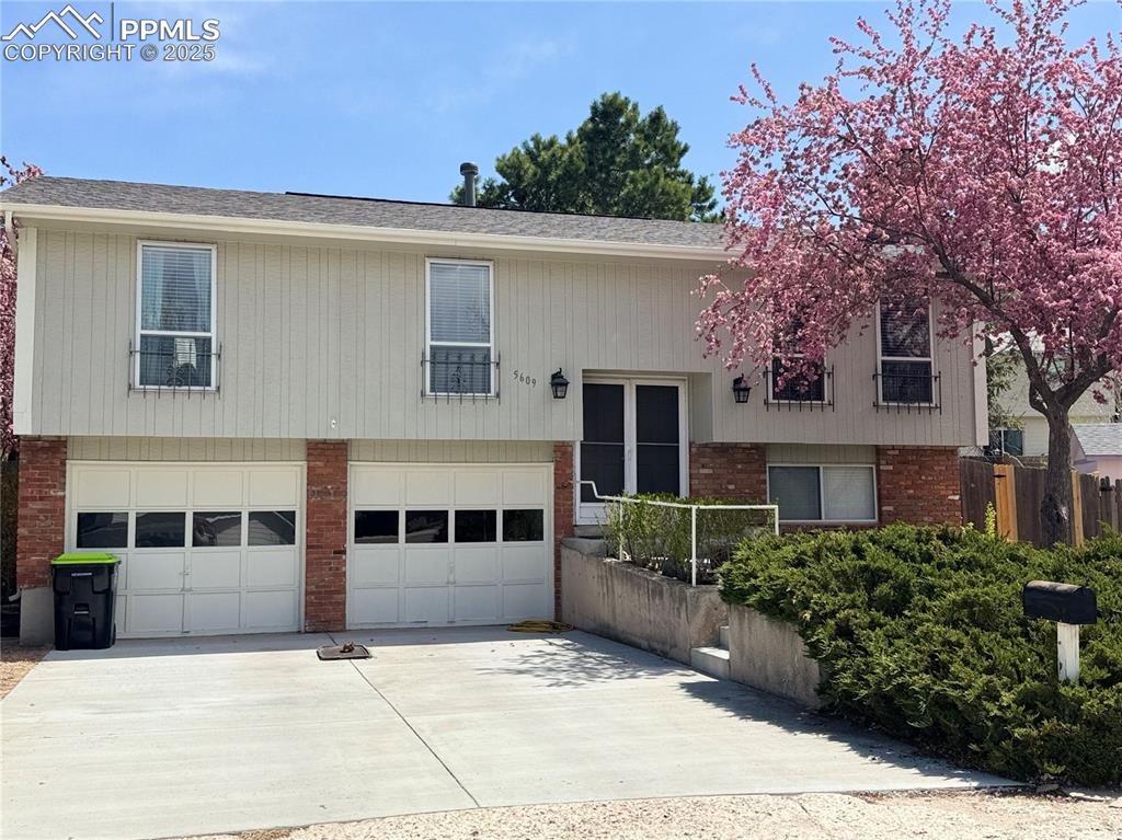 Caption: Bi-level home with driveway, a garage, brick siding, and roof with shingles