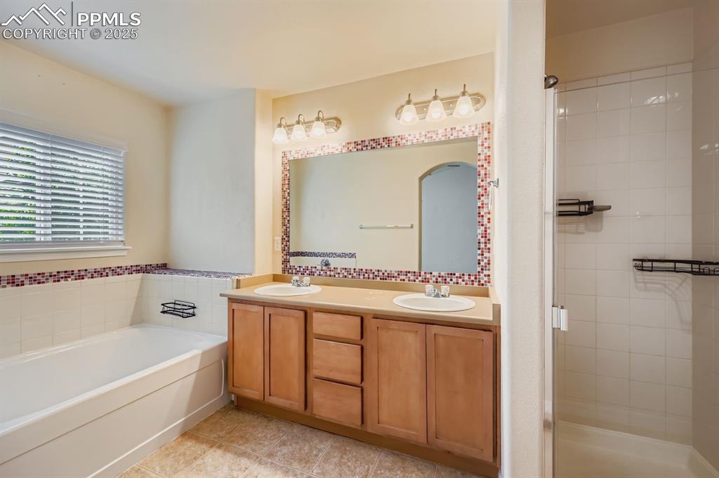 Image 9 of 10: Bathroom with a garden tub, a shower stall, double vanity, and light tile p