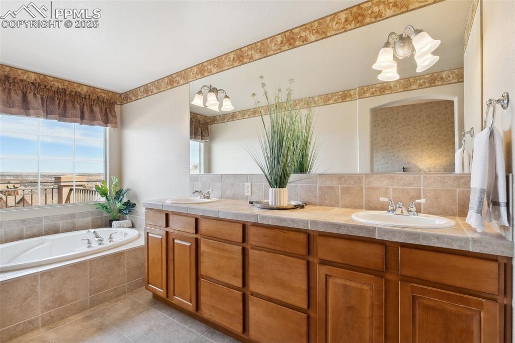 Image 25 of 44: Bathroom featuring a bath, double vanity, a sink, and backsplash