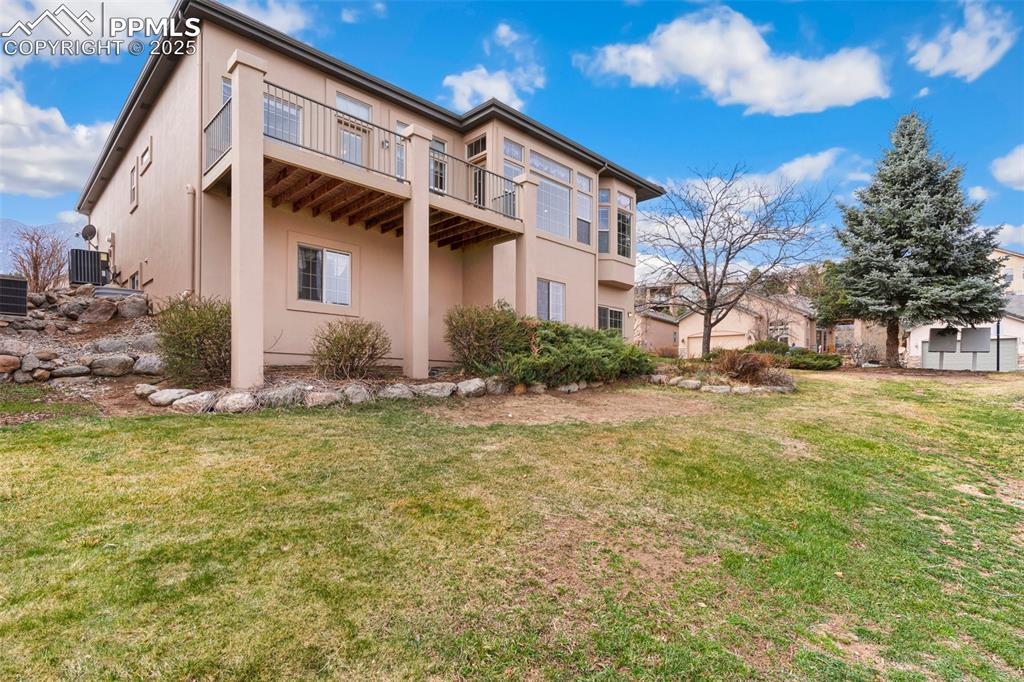 Image 40 of 44: Back of house featuring a balcony, a lawn, stucco siding, and central AC un