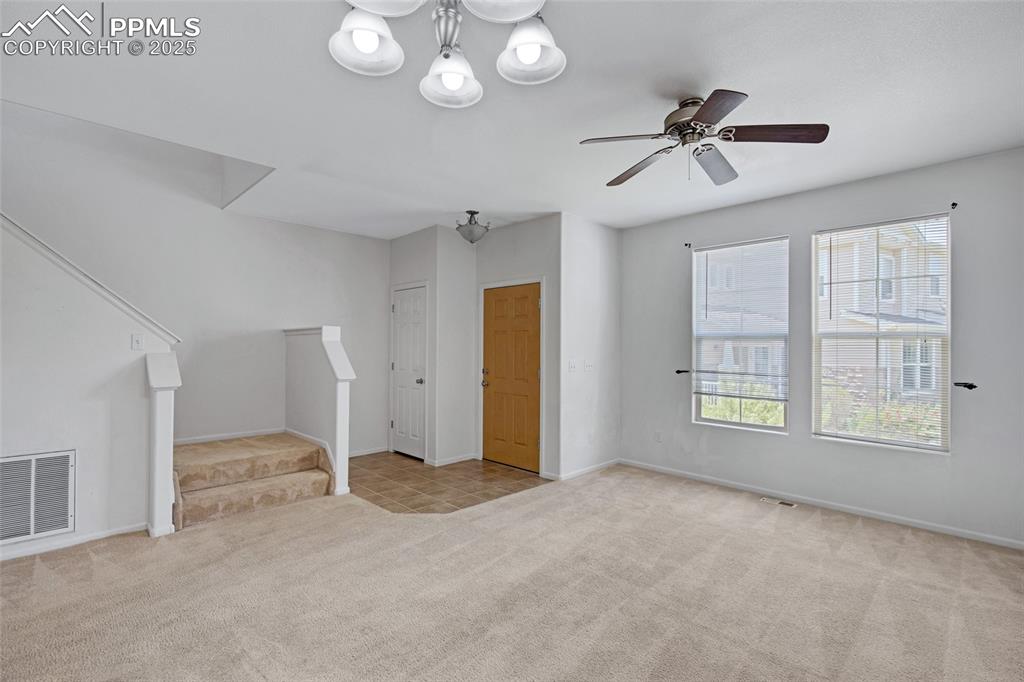 Image 6 of 24: Unfurnished living room with carpet floors, stairway, and ceiling fan