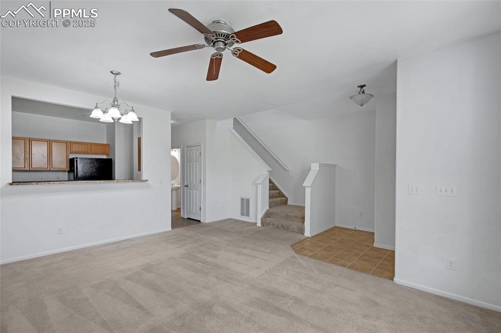 Image 7 of 24: Unfurnished living room with carpet, a ceiling fan, stairway, and a chandel