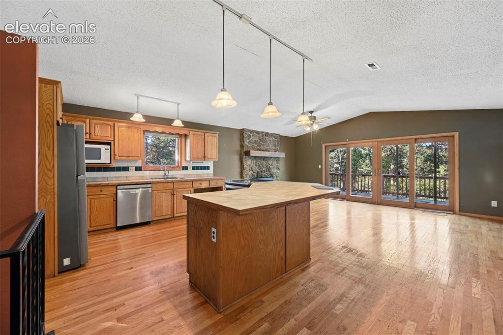 Image 14 of 47: Kitchen and open living area featuring wood-finish flooring, a stone firepl