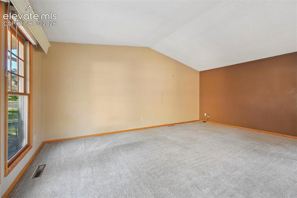 Image 15 of 47: Vaulted ceiling with an accent wall, wall-to-wall carpeting, and wood-frame