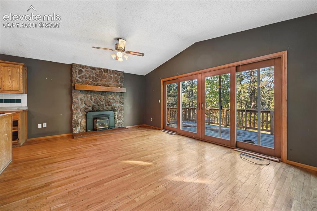 Image 21 of 47: Vaulted ceiling with a ceiling fan, stone-clad fireplace with wood mantle,