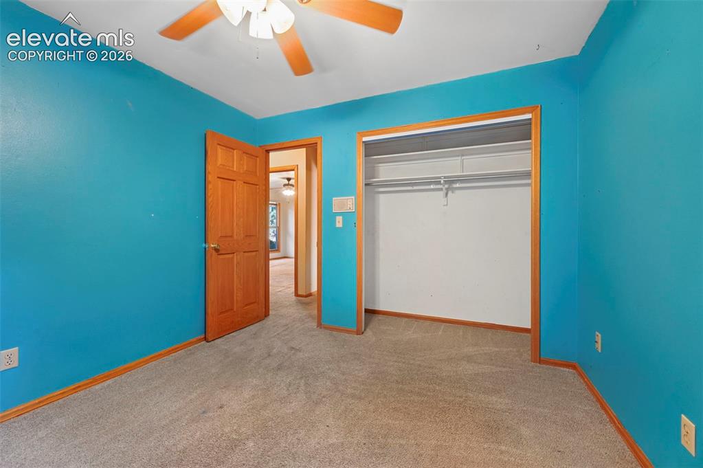 Image 28 of 47: Carpeted room featuring a ceiling fan, wood-finish door, and an open closet