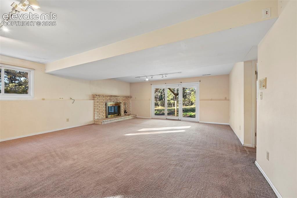 Image 34 of 47: Spacious lower-level room featuring a brick fireplace, carpeted flooring, t
