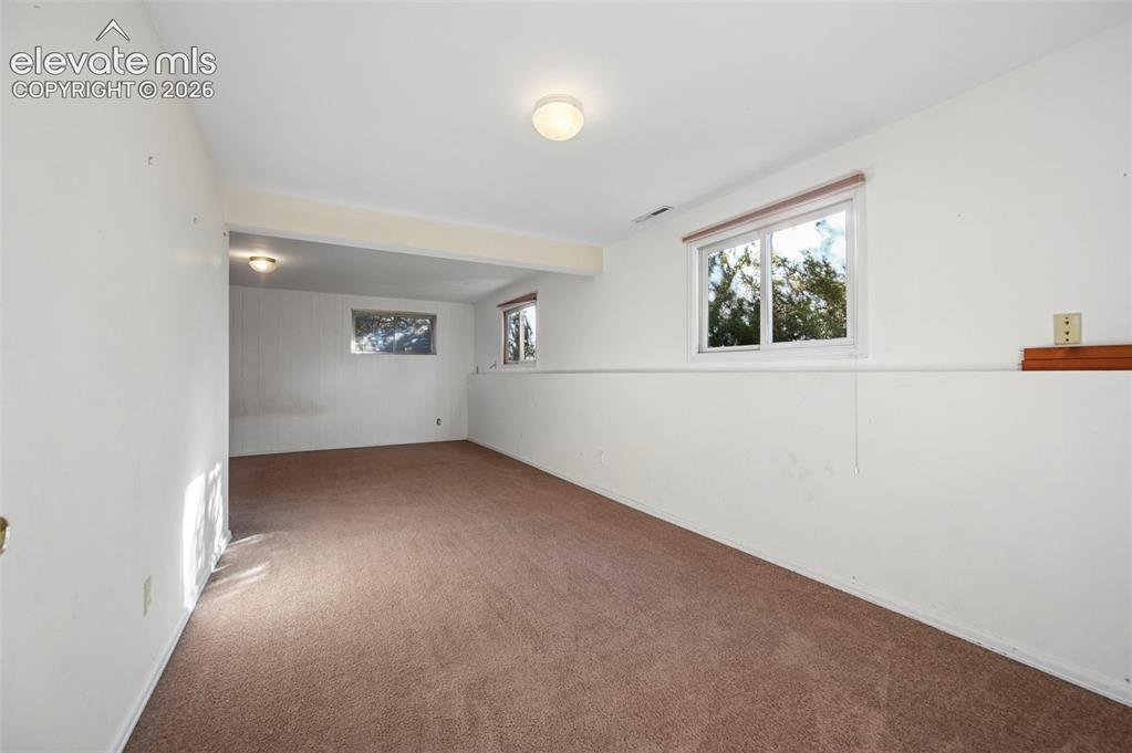 Image 40 of 47: Spacious room with carpeted flooring, multiple windows, and overhead lighti