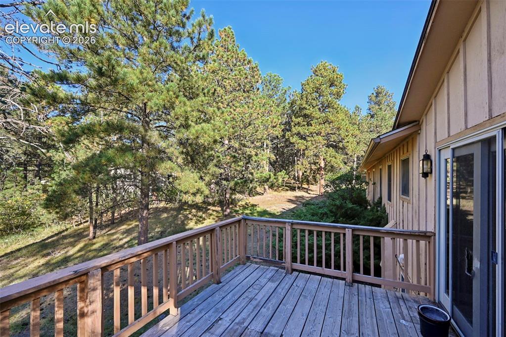 Image 43 of 47: Wood deck with wood railing, sliding glass door, exterior wall lantern, and