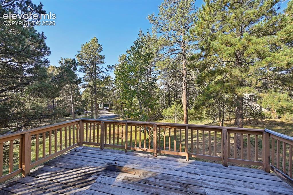 Image 44 of 47: Expansive outdoor deck with wood railing, surrounded by mature trees and na