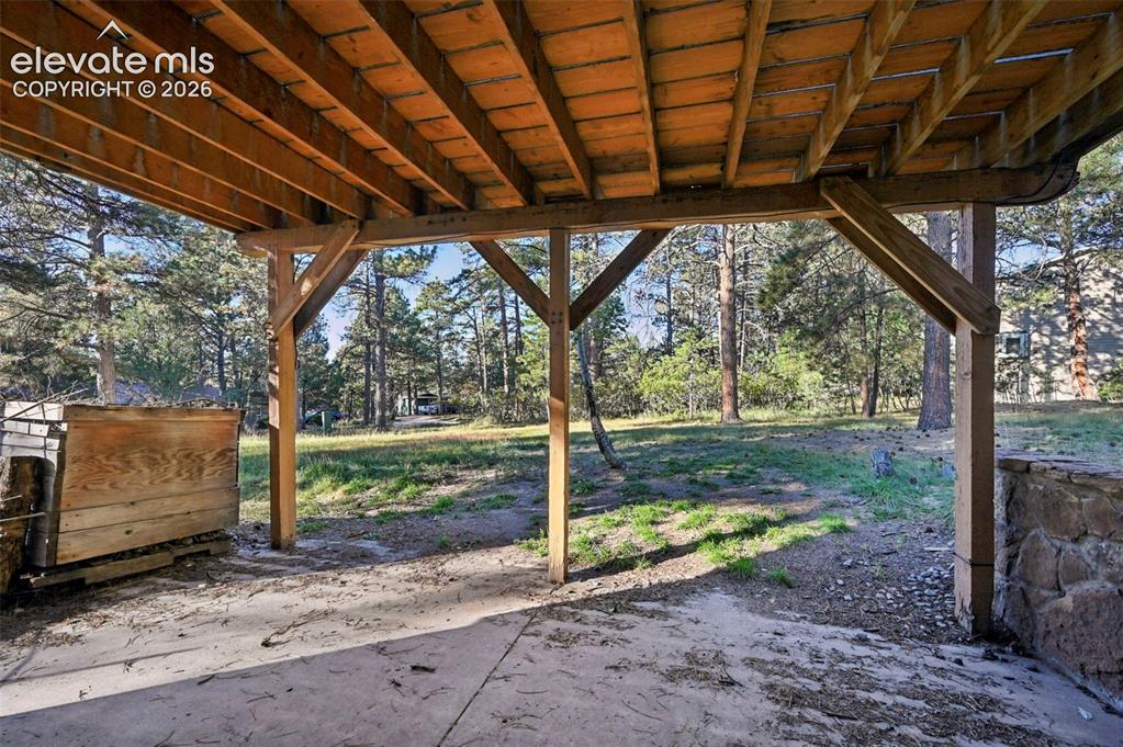 Image 46 of 47: Covered patio space with concrete flooring, supported by exposed wood beams