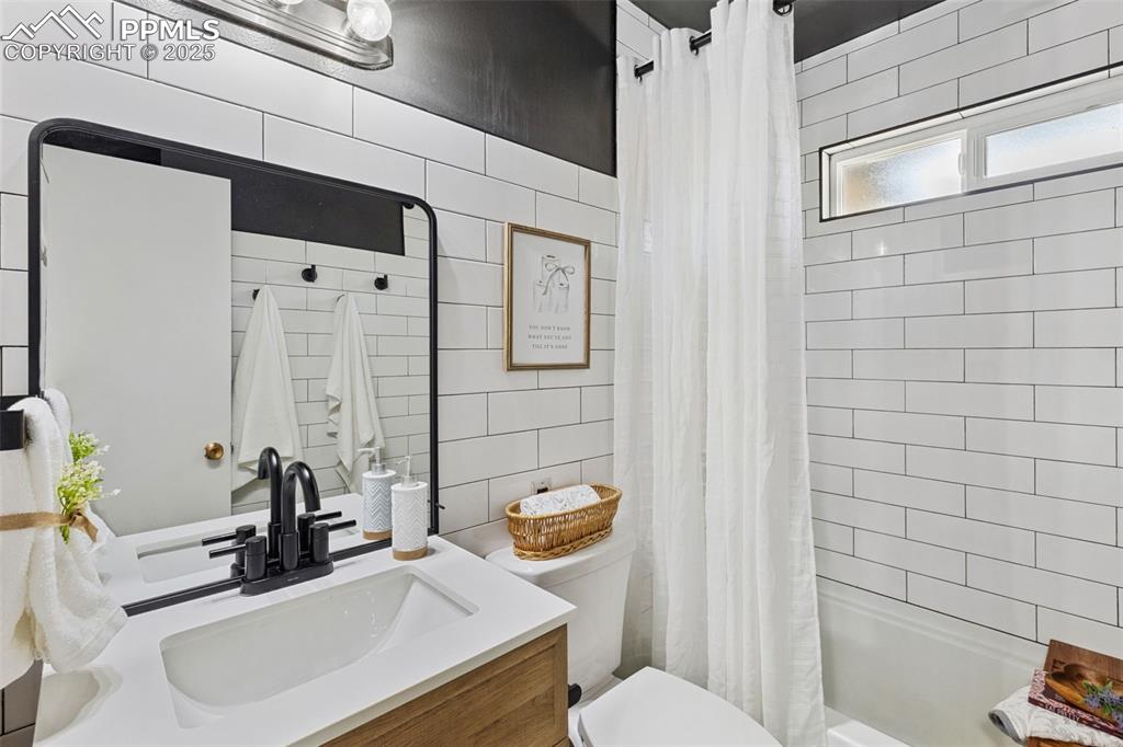 Image 15 of 38: Bathroom featuring tile walls, vanity, and shower / bath combination with c
