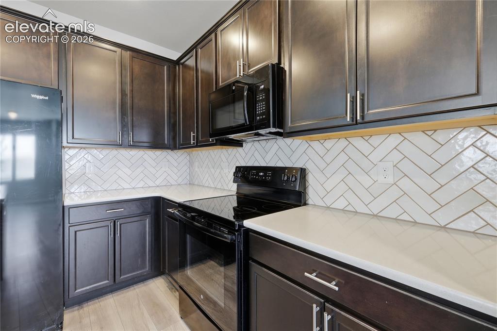 Image 14 of 42: Modern kitchen featuring dark wood cabinetry, white herringbone tile backsp