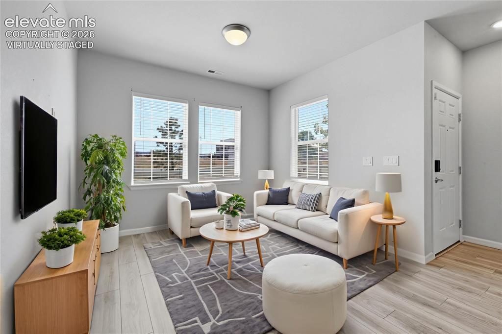 Image 2 of 42: Spacious living area featuring light wood-finish flooring, multiple windows