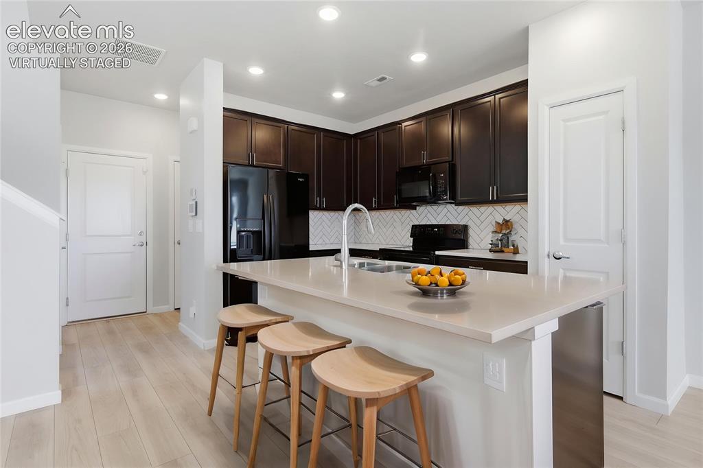 Image 7 of 42: Kitchen featuring dark wood cabinetry, a light-toned countertop island with