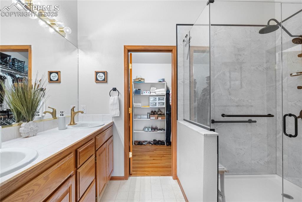 Image 25 of 49: Bathroom featuring double vanity, a shower stall, and a walk in closet