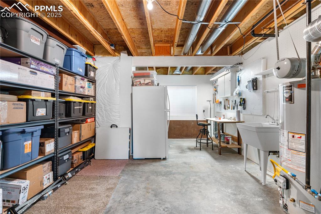 Image 37 of 49: Unfinished basement featuring freestanding refrigerator and gas water heate