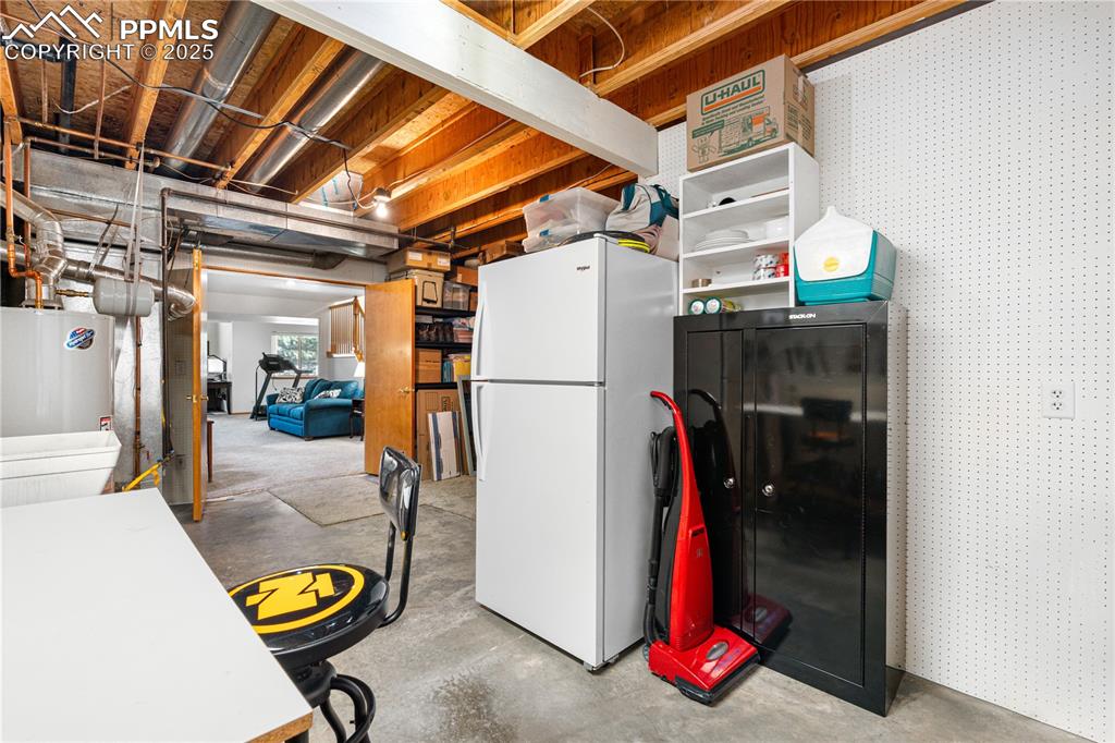 Image 38 of 49: Below grade area featuring freestanding refrigerator, water heater, and wal