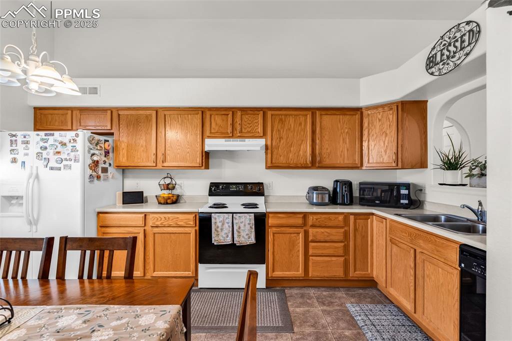 Image 4 of 20: Kitchen with black appliances, light countertops, a chandelier, and brown c