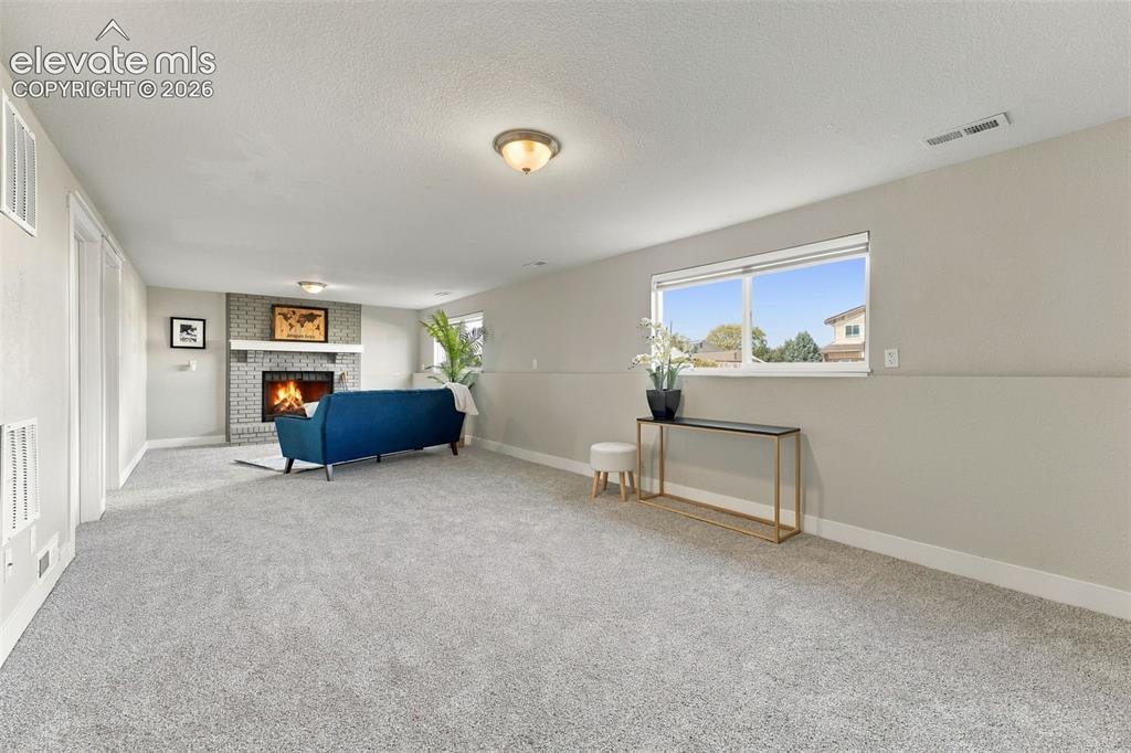 Image 24 of 46: Spacious room featuring light-colored carpeting, a brick-surround fireplace
