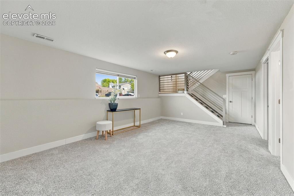 Image 27 of 46: Carpeted living area featuring a window, modern railing staircase, and rece