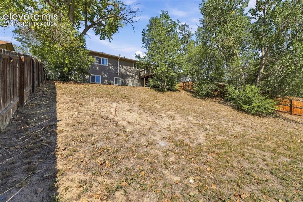 Image 38 of 46: Expansive sloped backyard featuring mature trees, partial fencing, and a tw