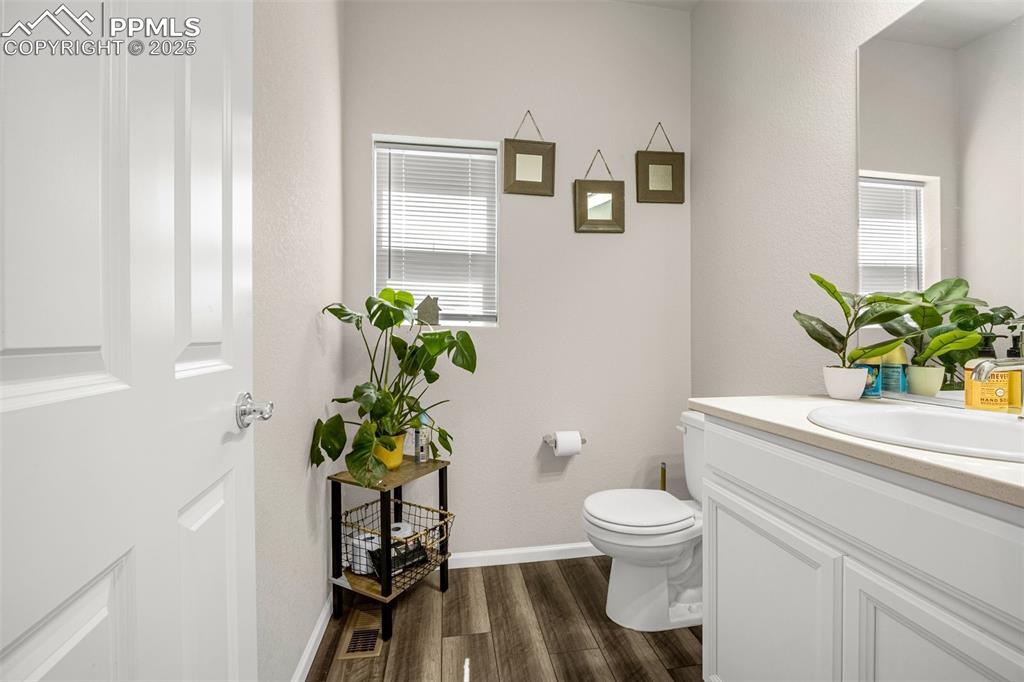 Image 13 of 35: Half bathroom with vanity, wood finished floors, and plenty of natural ligh