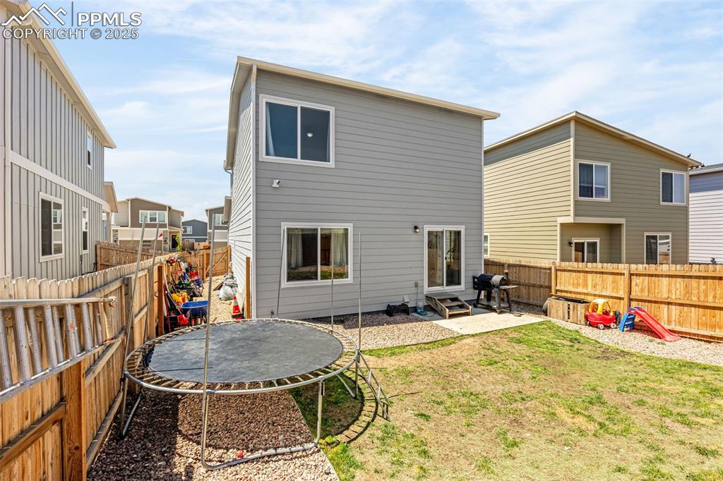 Image 25 of 35: Rear view of house with a trampoline, a fenced backyard, a patio, and entry