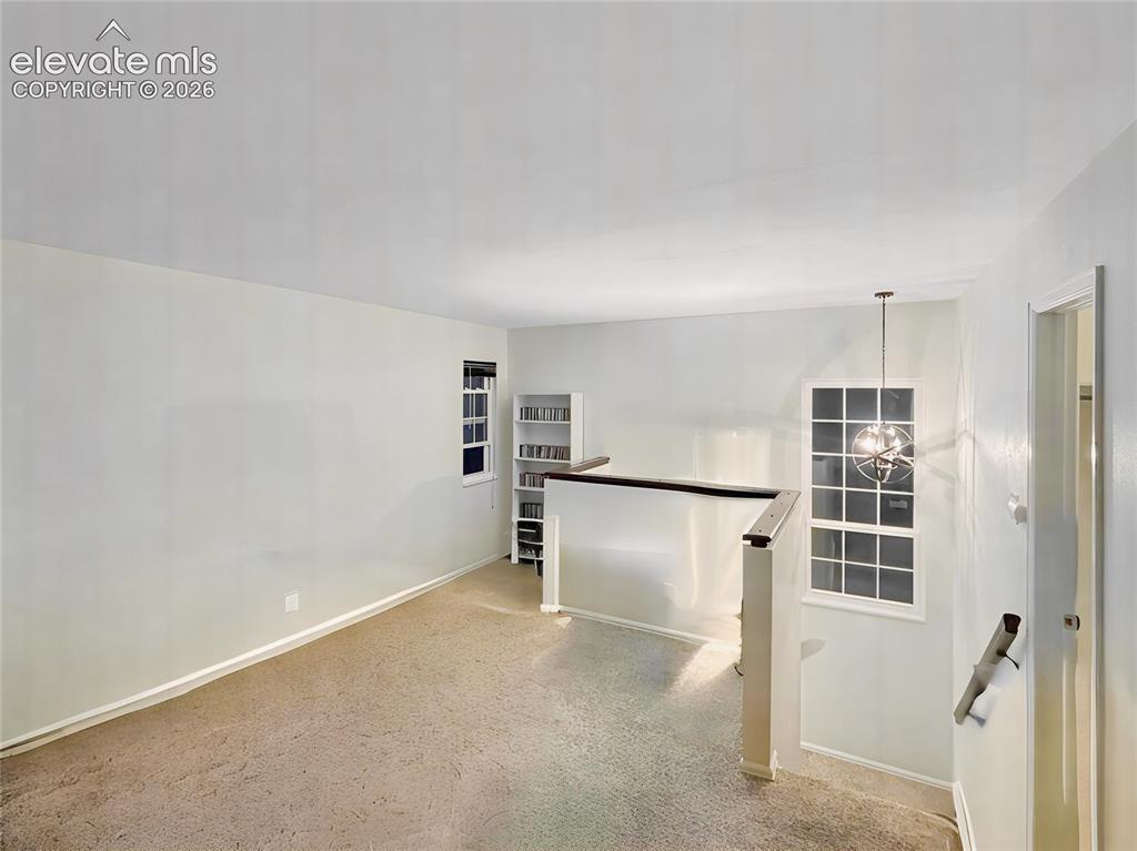 Image 22 of 44: Carpeted loft area with a contemporary chandelier, white trim, and a built-