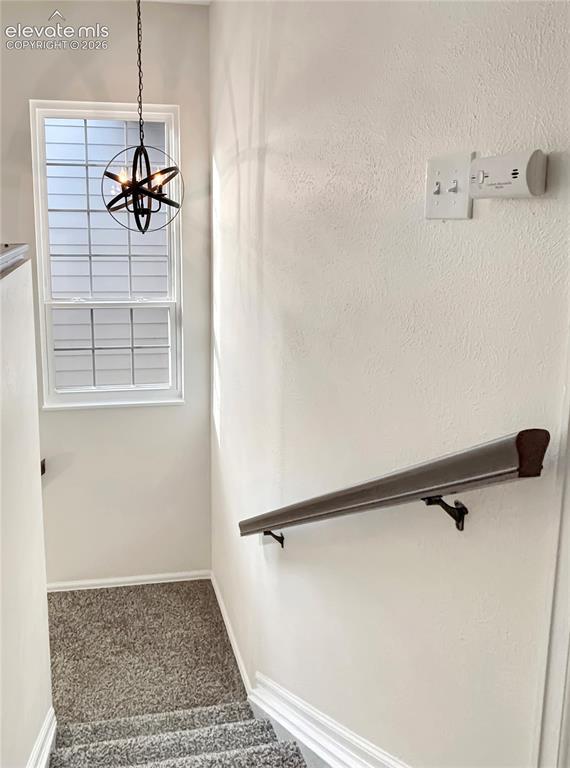 Image 23 of 44: Stairwell featuring a contemporary chandelier, a window with horizontal bli