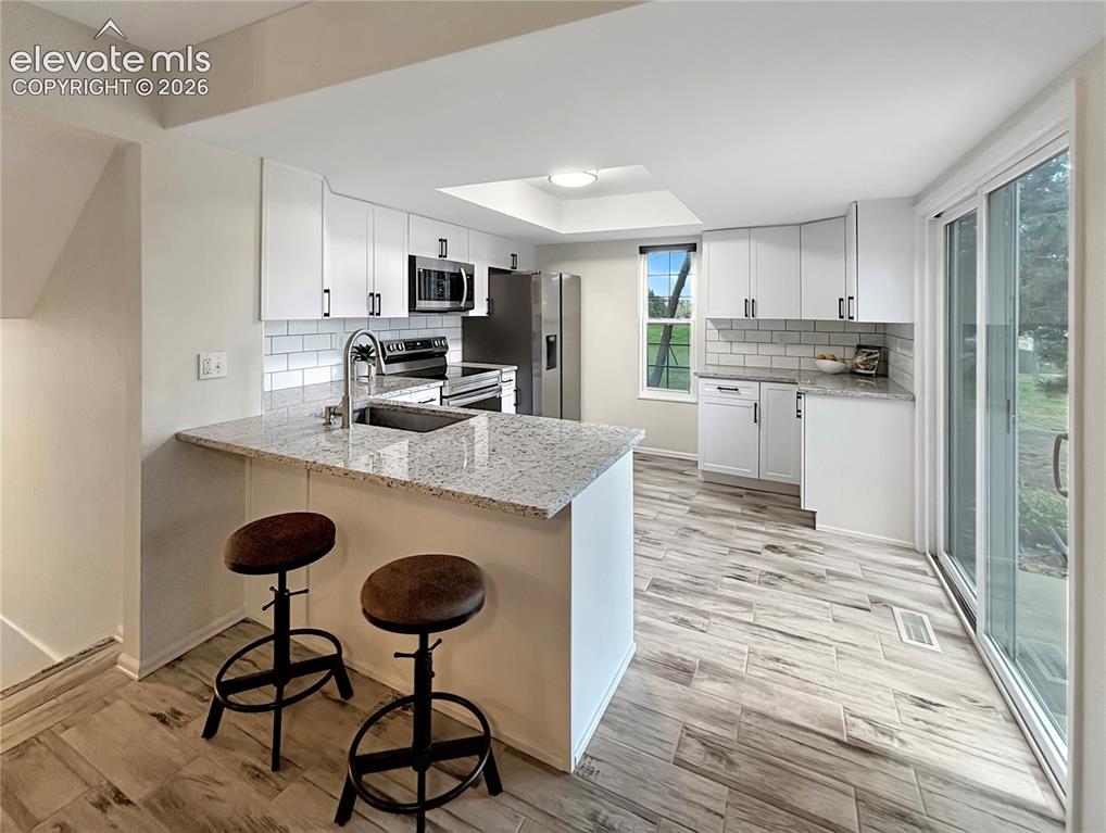 Image 3 of 44: Bright kitchen featuring white cabinetry, granite countertops, subway tile