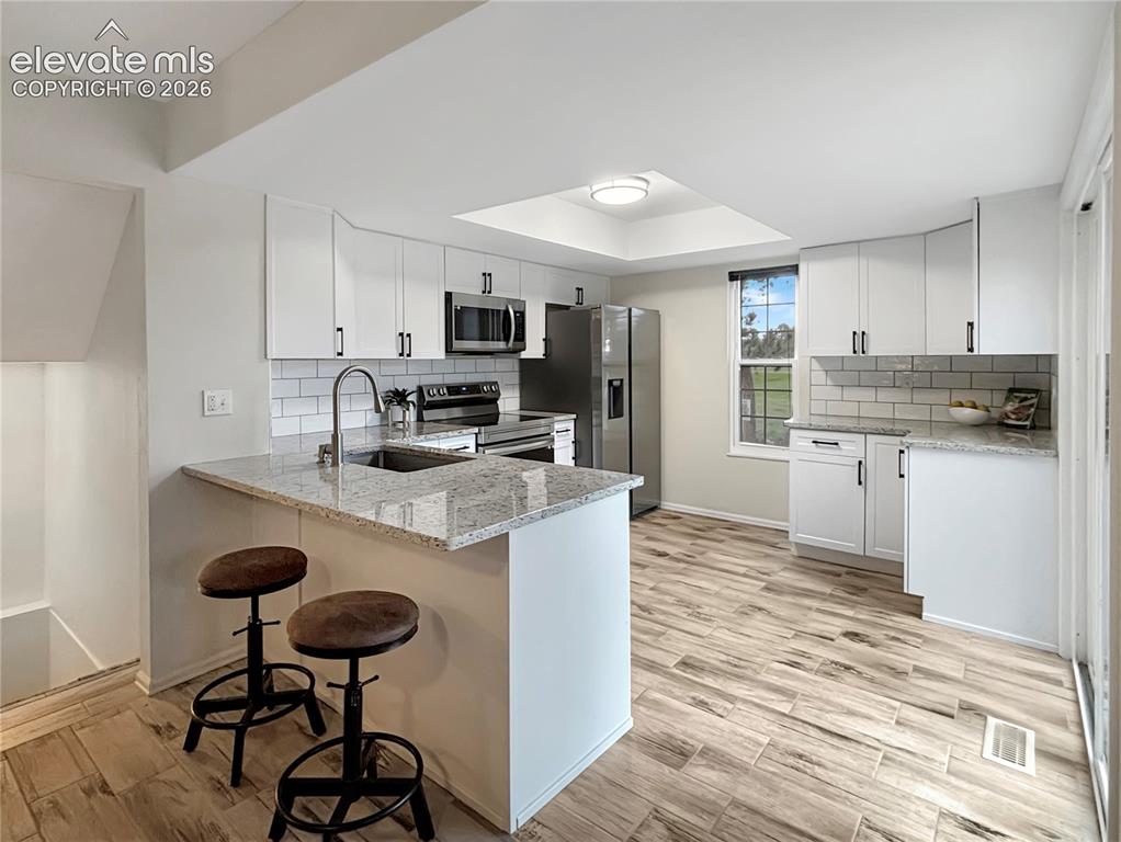 Image 8 of 44: Modern kitchen featuring light wood-finish flooring, white cabinetry, grani