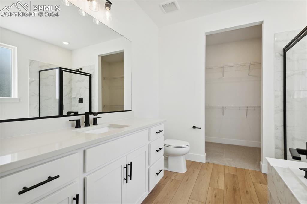 Image 7 of 15: Bathroom with toilet, vanity, an enclosed shower, and hardwood / wood-style