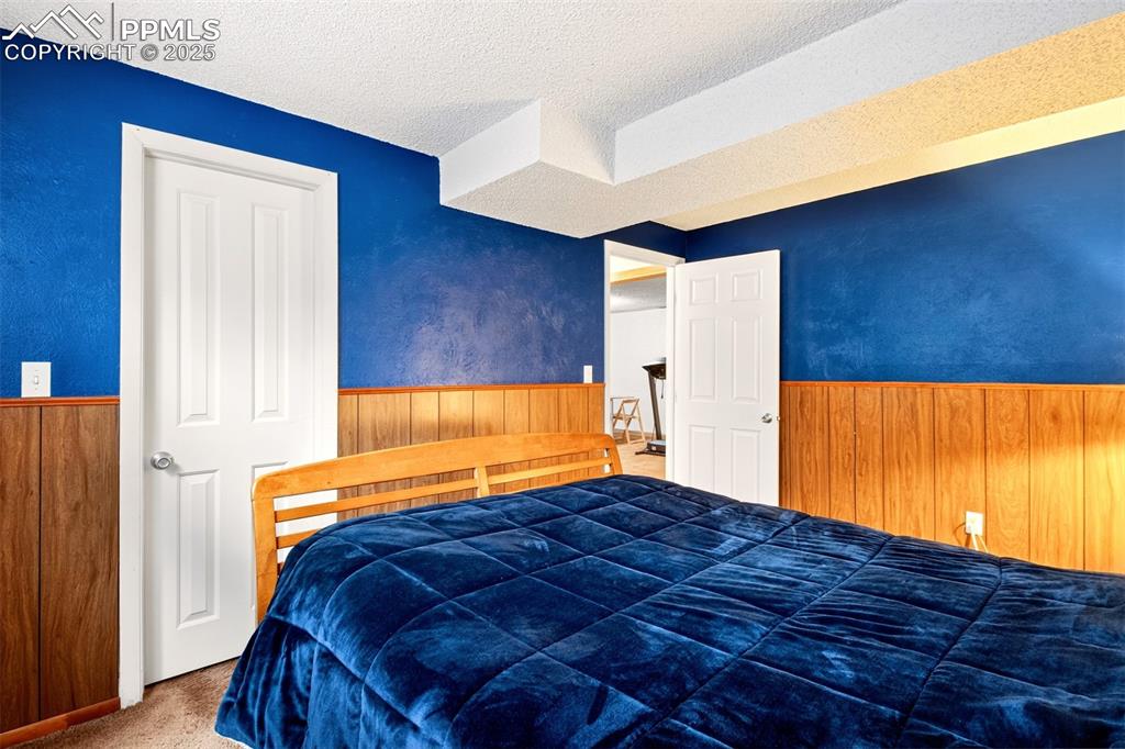Image 34 of 37: Bedroom featuring carpet flooring, a textured ceiling, wood walls, and wain