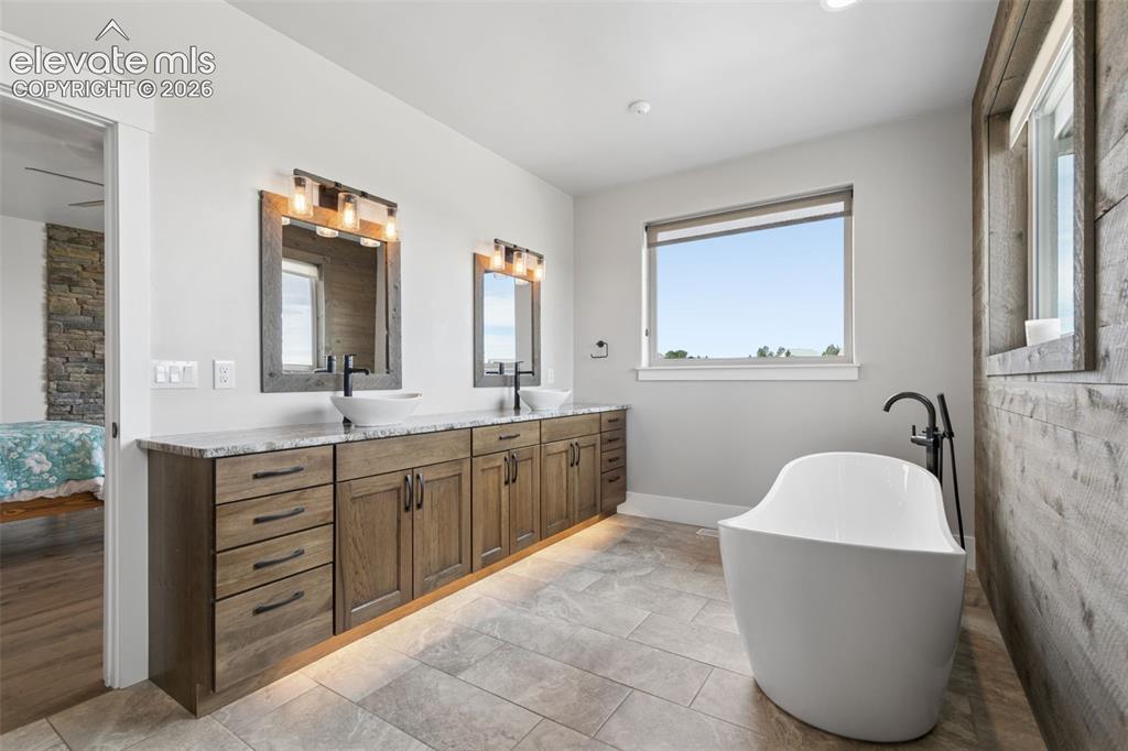 Image 27 of 50: Dual vanity with wood-finish cabinetry, under-cabinet lighting, and stone c