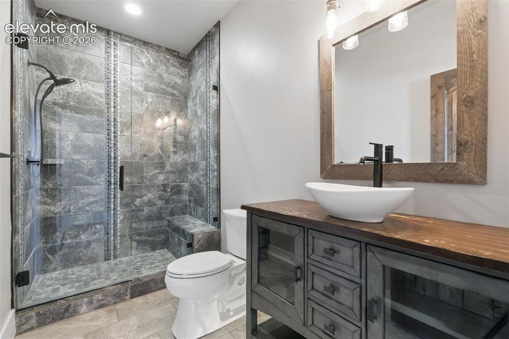Image 28 of 50: Glass-enclosed shower with stone-look tile, a built-in bench, and a rain sh