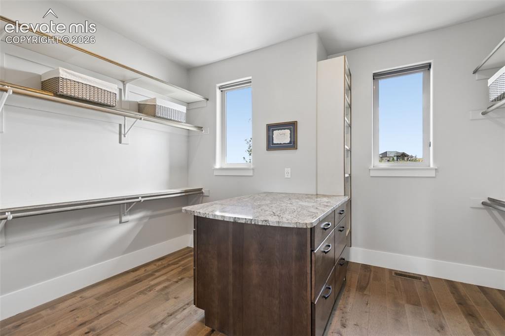 Image 30 of 50: Custom closet island with stone-finish countertop, wood-finish flooring, an