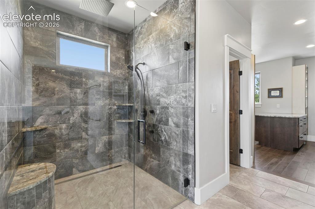 Image 38 of 50: Glass-enclosed shower with full tile surround, integrated shower bench, and