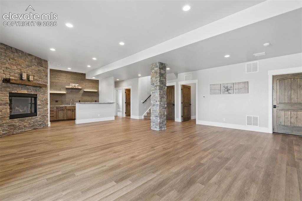 Image 39 of 50: Spacious room featuring wood-finish flooring, a stone-clad fireplace, and a