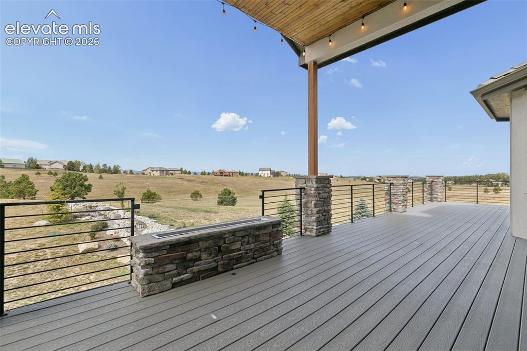 Image 44 of 50: Expansive deck with composite decking, stone-clad pillars, and a built-in s