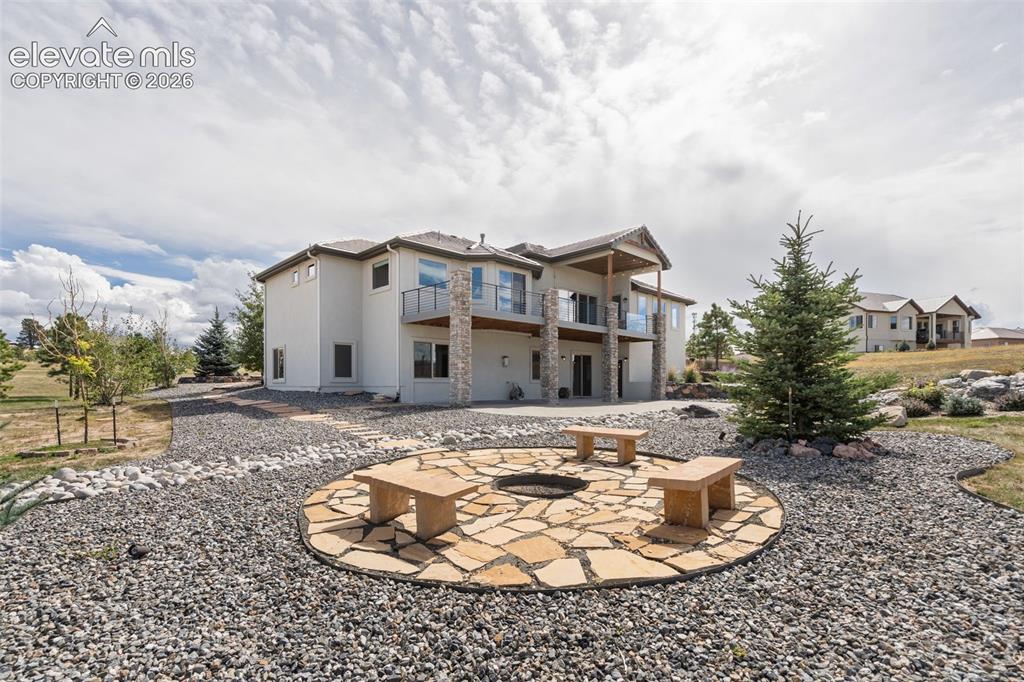 Image 45 of 50: Expansive backyard featuring a stone patio with built-in fire pit, multiple